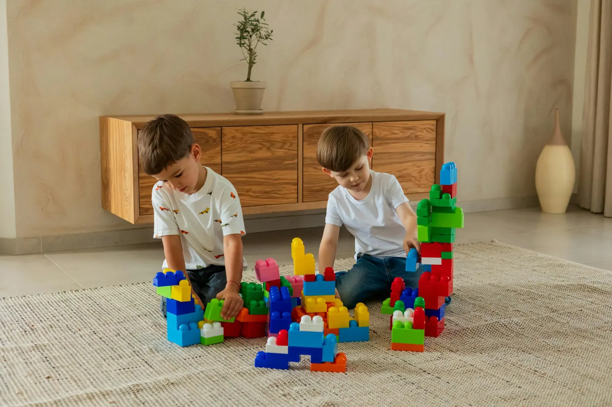 Dos niños disfrutan construyendo con bloques de juguetes de colores en un acogedor ambiente de sala de estar.