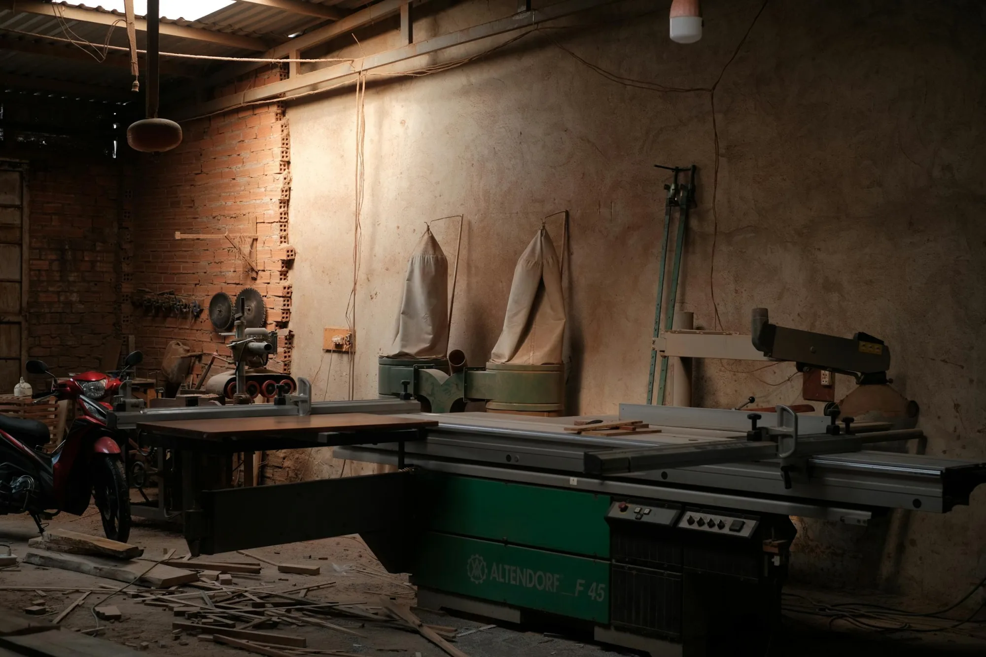 Un taller rústico con poca luz, equipado con una sierra Altendorf F45 y herramientas industriales.