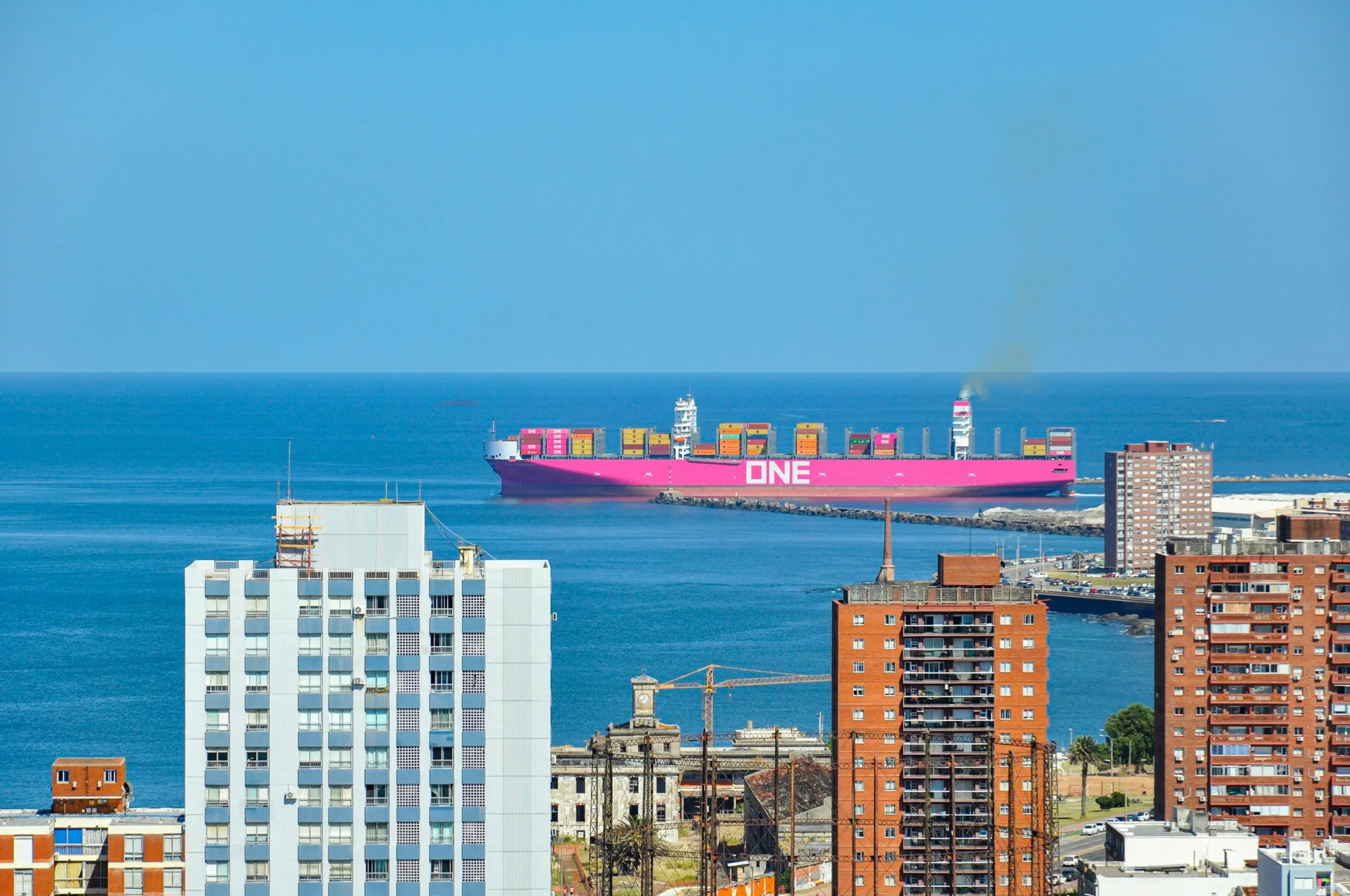 Large pink cargo ship sailing in blue ocean near city.