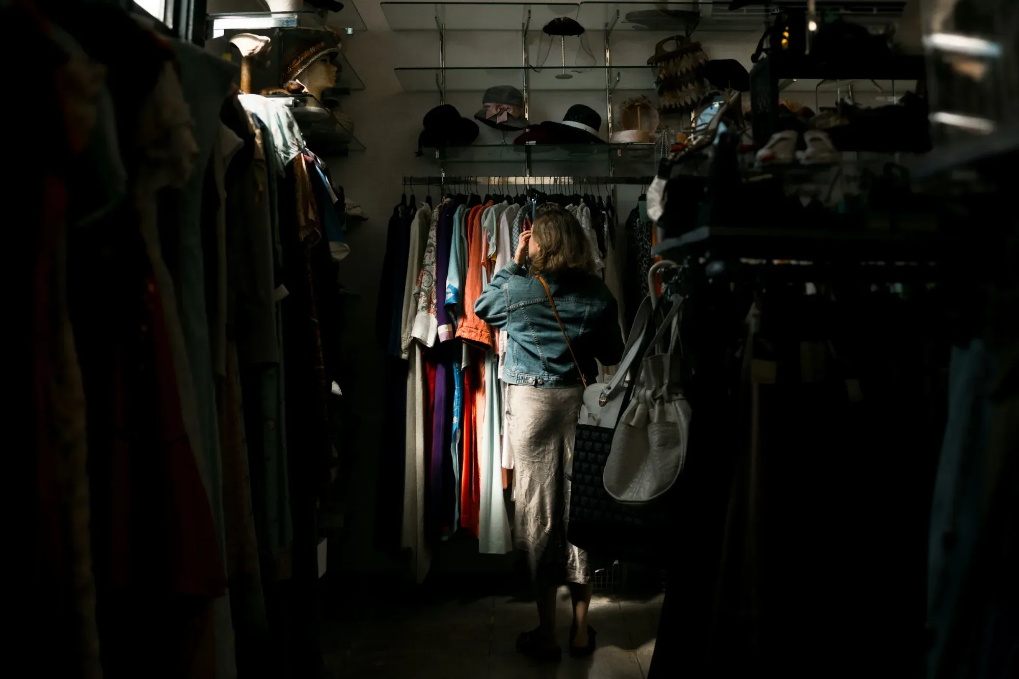 Woman browsing clothes rack in dimly lit store.